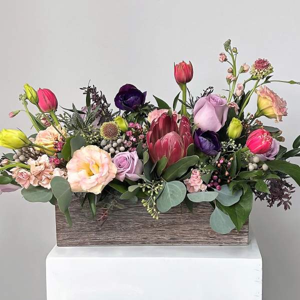 Mixed bouquet of tulips, roses, and protea in a wooden box