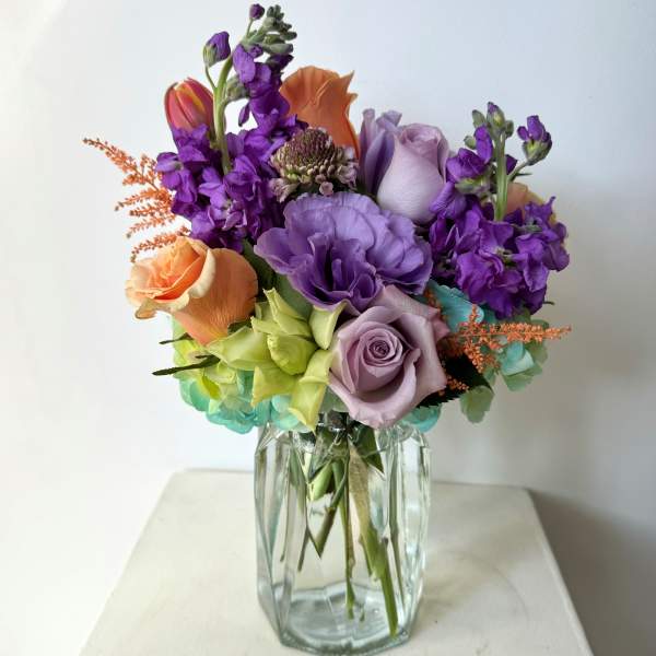 Colorful bouquet of roses and purple flowers in a clear glass vase