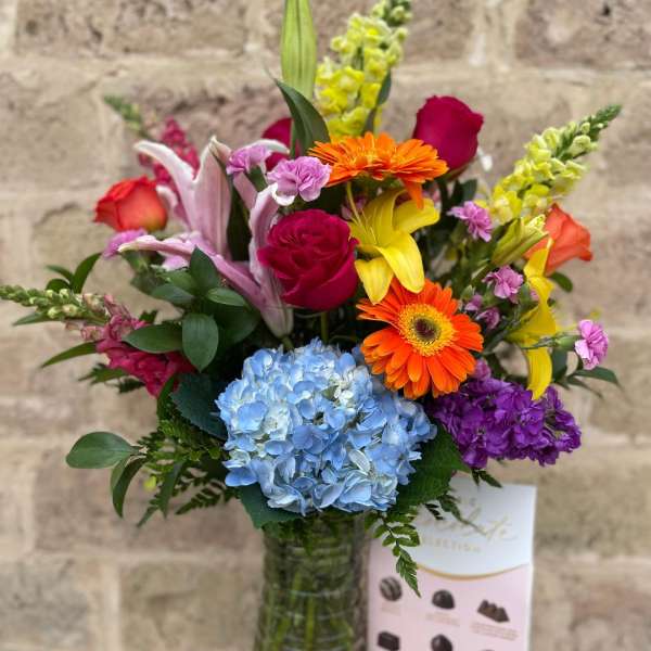 Colorful mixed bouquet in a glass vase with roses, lilies, gerbera daisies, and hydrangea