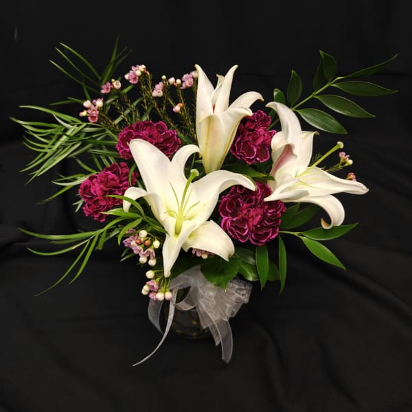 White lilies and magenta carnations in a glass vase with ribbon