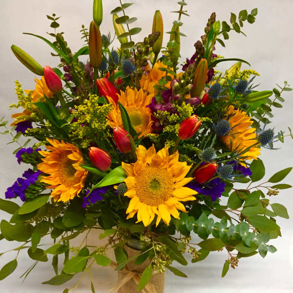 Bouquet of sunflowers, tulips, and purple accents in a burlap-wrapped vase