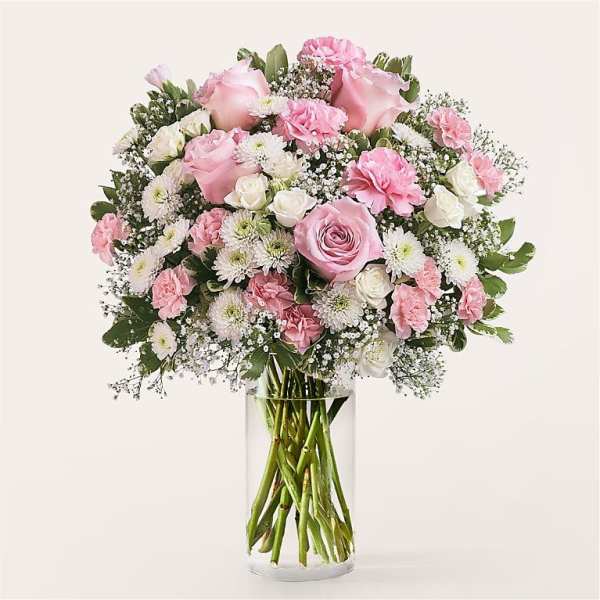 Pink and white bouquet of roses, carnations, and daisies in a clear glass vase