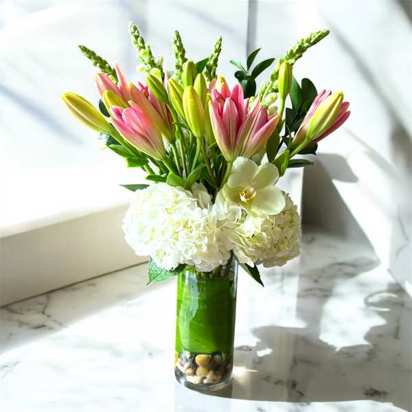 Pink lilies and white hydrangeas in a tall glass vase
