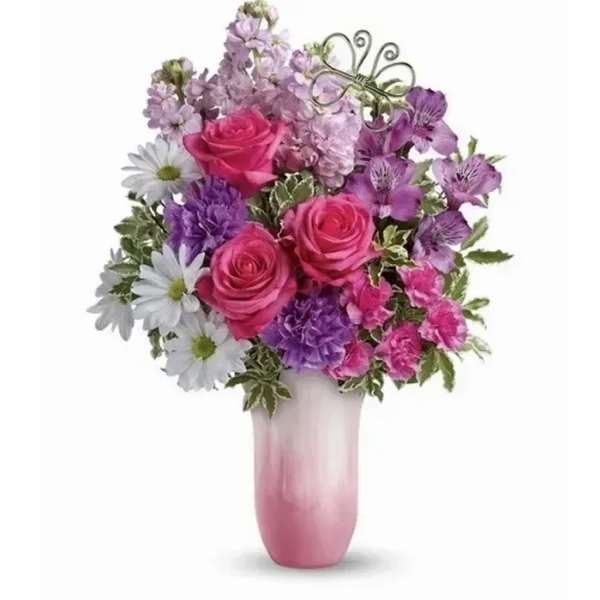 Pink roses, purple blooms, and white daisies in a pink ombré vase with a metal butterfly accent