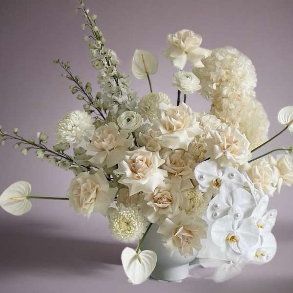 Cream and white floral arrangement in a white vase with orchids and roses