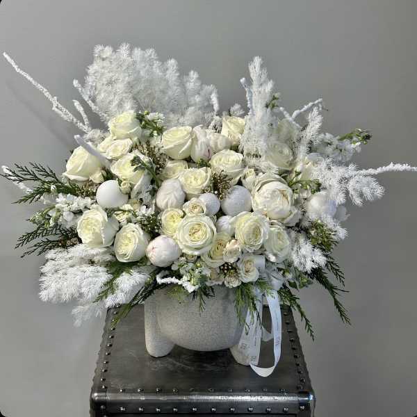 White rose arrangement in a textured vase with feathery white accents