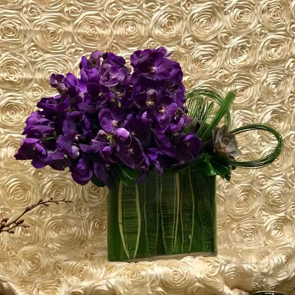 Purple orchid arrangement in a green rectangular vase