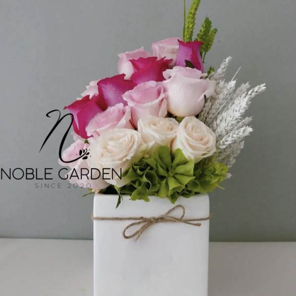 Pink and white roses arranged in a white box with twine