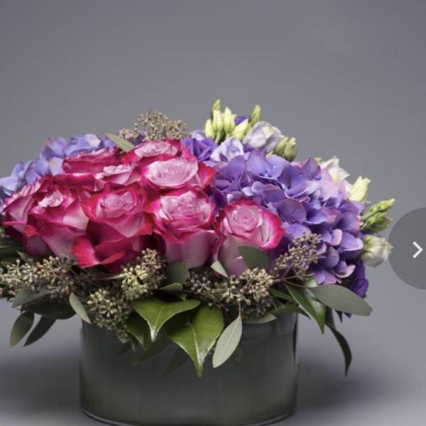 Pink roses and purple hydrangeas arranged in a dark round box