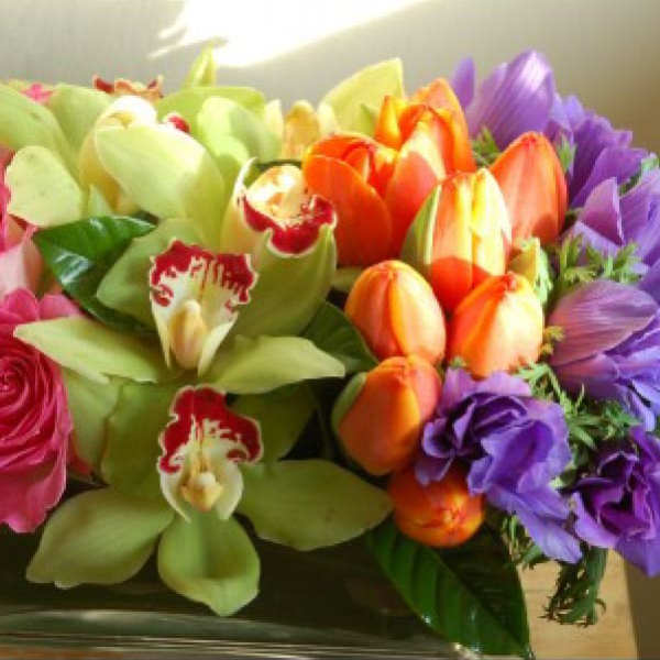 Bouquet of pink roses, green orchids, orange tulips, and purple flowers in a glass vase