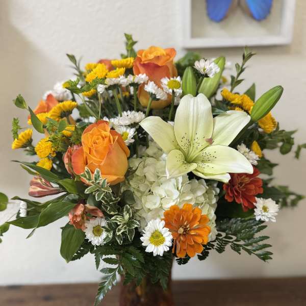 Orange roses and white lilies in a glass vase with mixed daisies