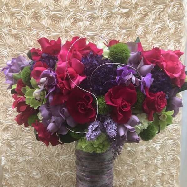 Tall bouquet of red, purple, and green flowers in a wrapped vase