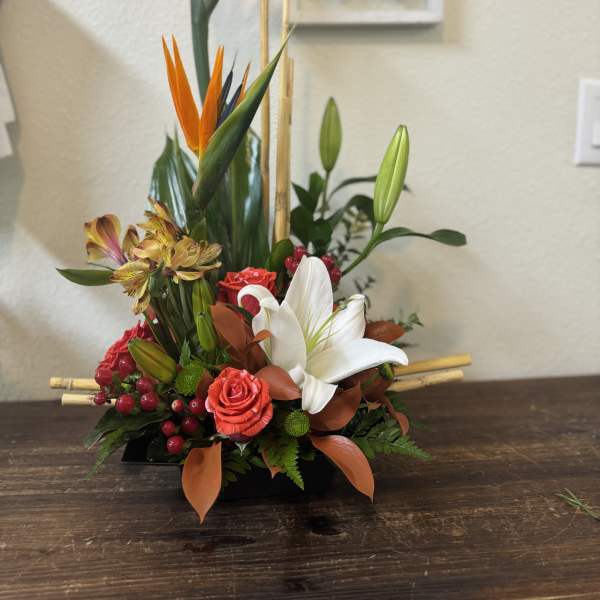 Tropical floral arrangement with white lilies and orange bird-of-paradise in a black container