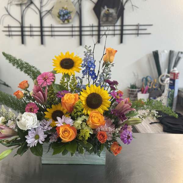 Mixed bouquet with sunflowers, roses, lilies, and daisies in a rectangular vase