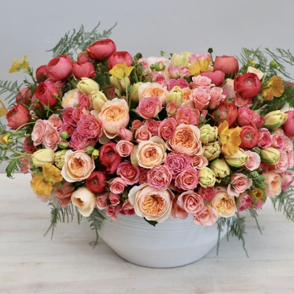 Large bouquet of pink, peach, and red roses in a white bowl vase