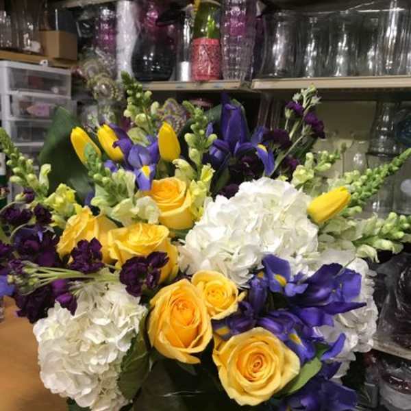 Bouquet of yellow roses, white hydrangeas, and purple flowers in a vase