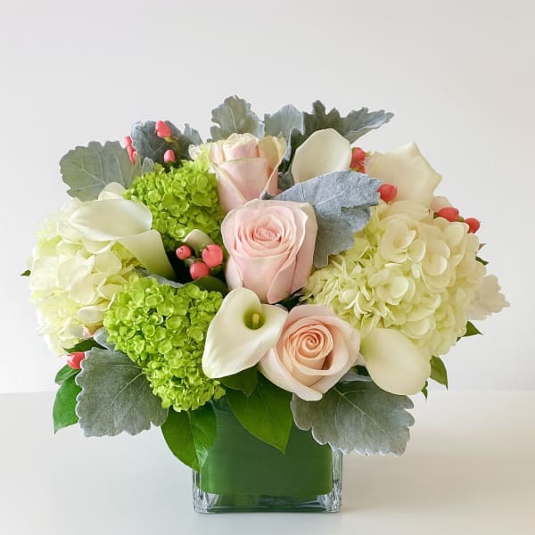 Bouquet of pale roses, white calla lilies, and green hydrangeas in a glass vase