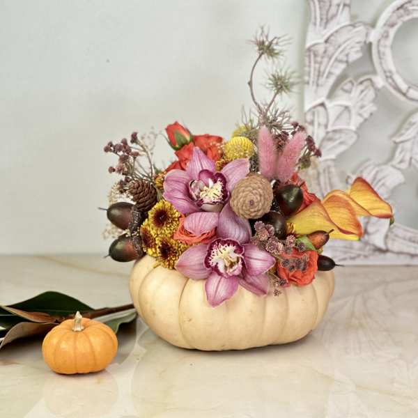 Floral arrangement in a pumpkin-shaped container with a small pumpkin beside it
