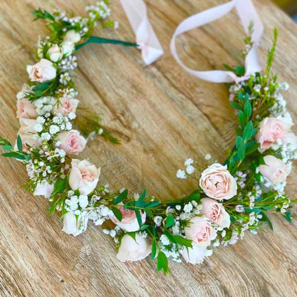Floral crown with pale pink roses and white filler flowers on a wooden surface