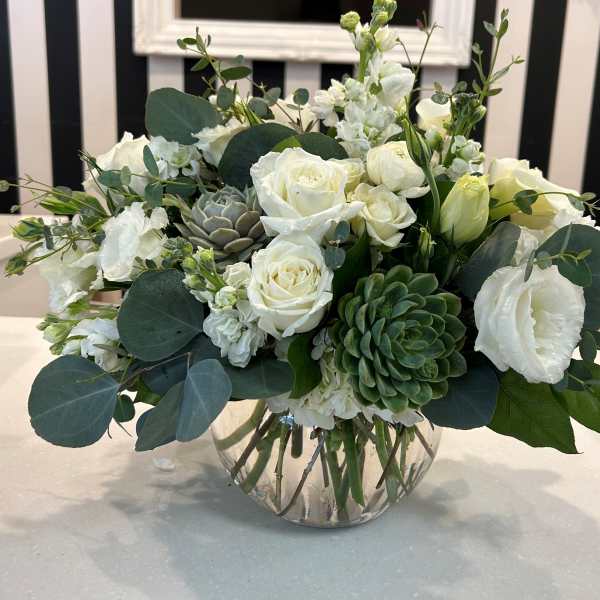 White roses and greenery arranged in a clear glass vase with succulents.