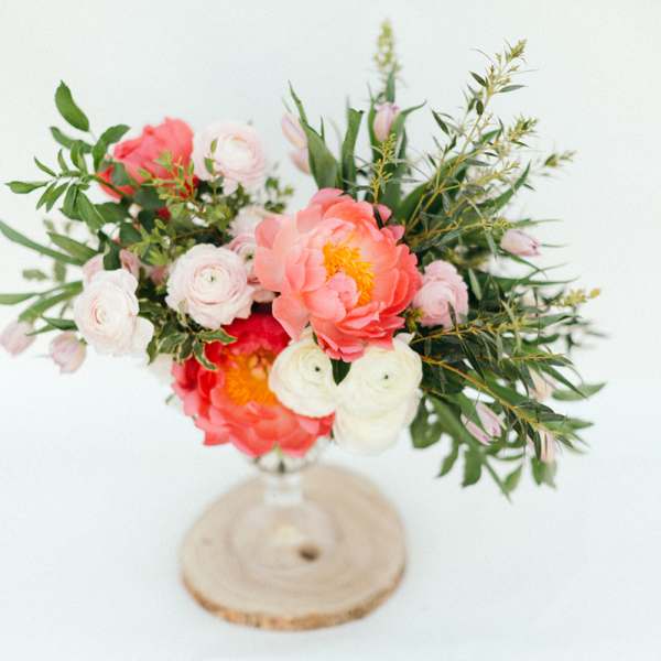 Pink and white floral arrangement in a clear vase on a wood slice base