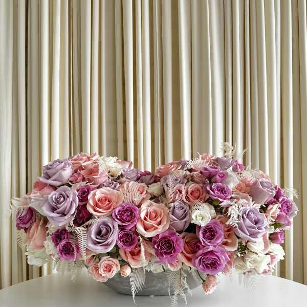 Low centerpiece of pink, lavender, and white roses in a gray bowl on a white table