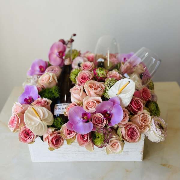 Pink roses and orchids arranged around a wine bottle in a white box