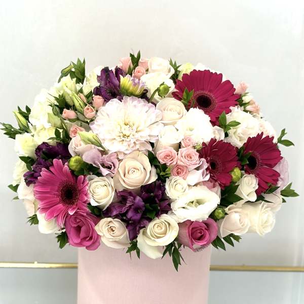 Round bouquet of pink, white, and purple flowers in a pink box
