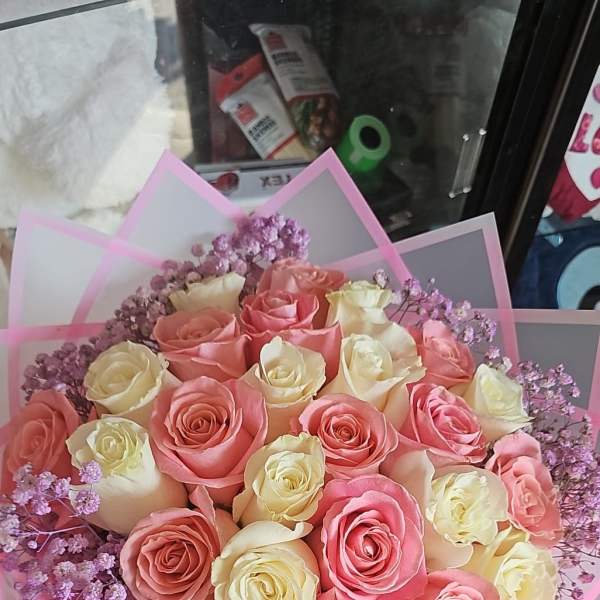 Round bouquet of pink and cream roses with lavender filler flowers wrapped in pink translucent paper