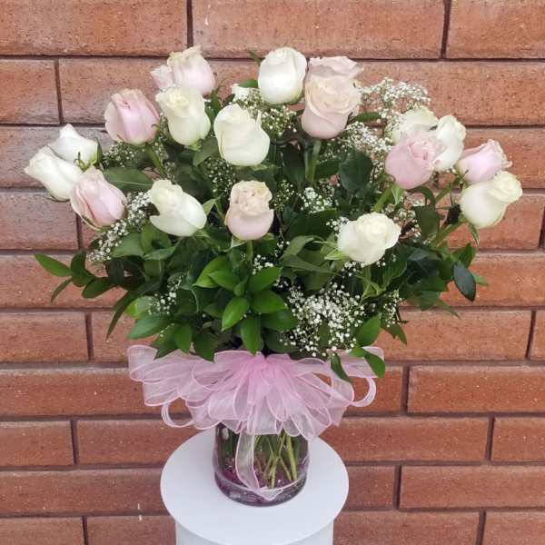 Pink and white roses in a glass vase with a pink ribbon bow