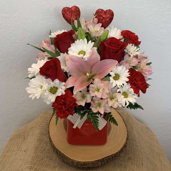Bouquet of red roses, pink lilies, and white daisies in a red vase with heart picks