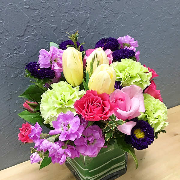Colorful bouquet in a square glass vase with tulips, carnations, and purple blooms