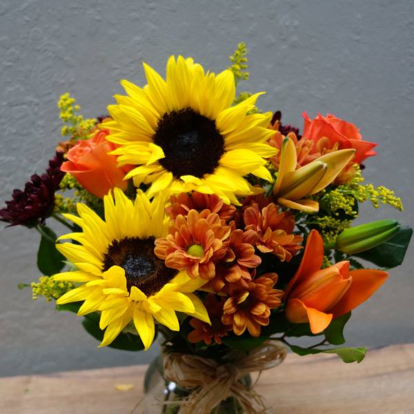 Bouquet of sunflowers, orange lilies, and mums in a glass vase