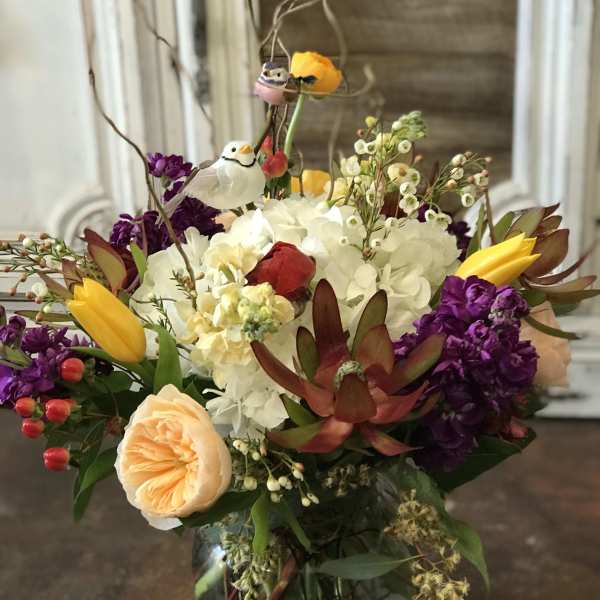 Mixed bouquet in a glass vase with yellow tulips, white hydrangea, and purple blooms