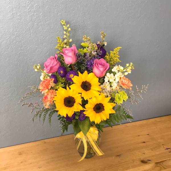 Bouquet of sunflowers, pink roses, and mixed flowers in a glass vase