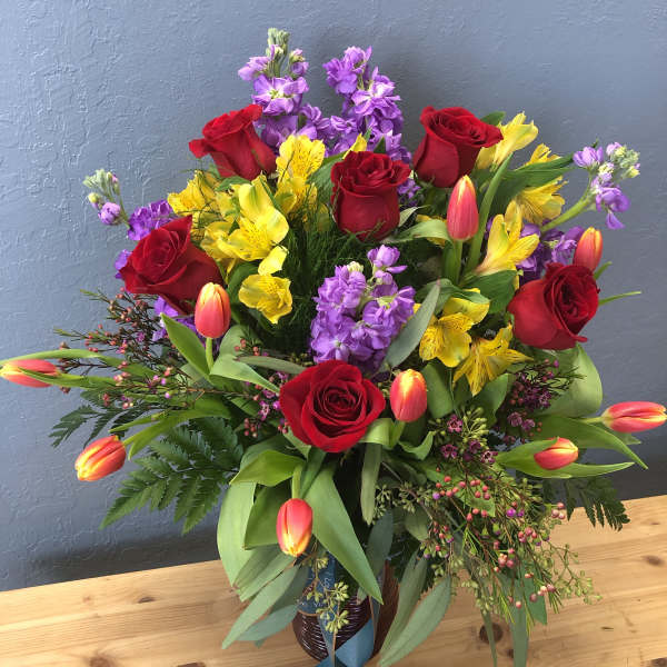 Bouquet of red roses, yellow alstroemeria, and purple flowers in a vase