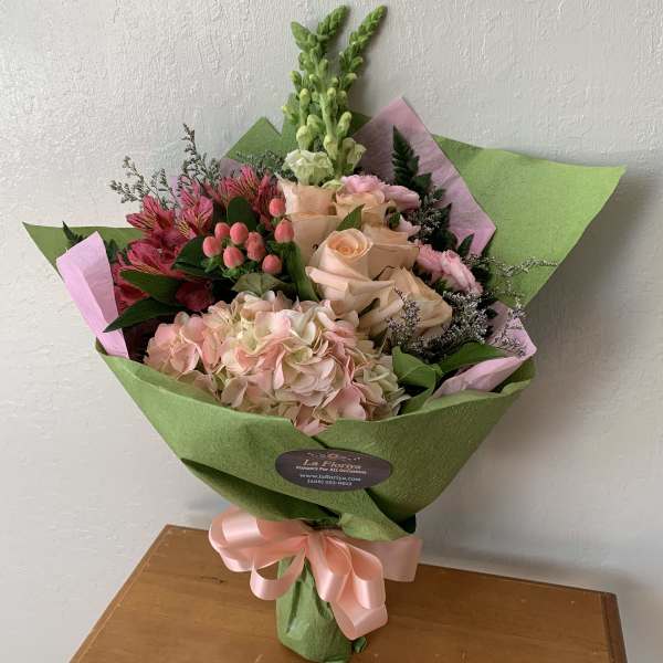 Bouquet of pink and peach flowers wrapped in green paper with a pink ribbon
