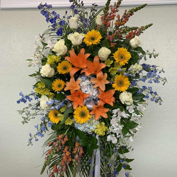 Tall standing floral spray with orange lilies, yellow daisies, and blue flowers