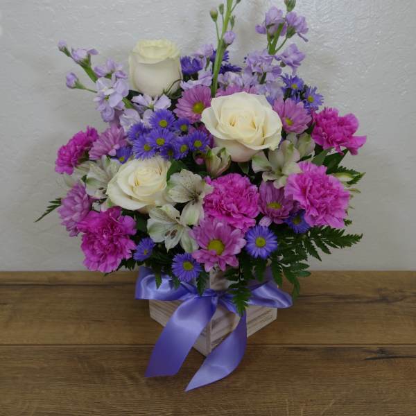Mixed bouquet of white roses, pink carnations, and purple daisies in a ribboned box