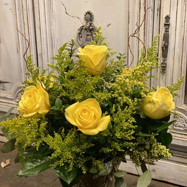 Yellow roses arranged in a clear glass vase with airy green filler