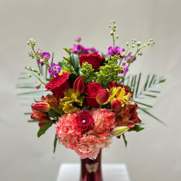 Mixed bouquet of red roses, pink hydrangeas, and yellow flowers in a red vase