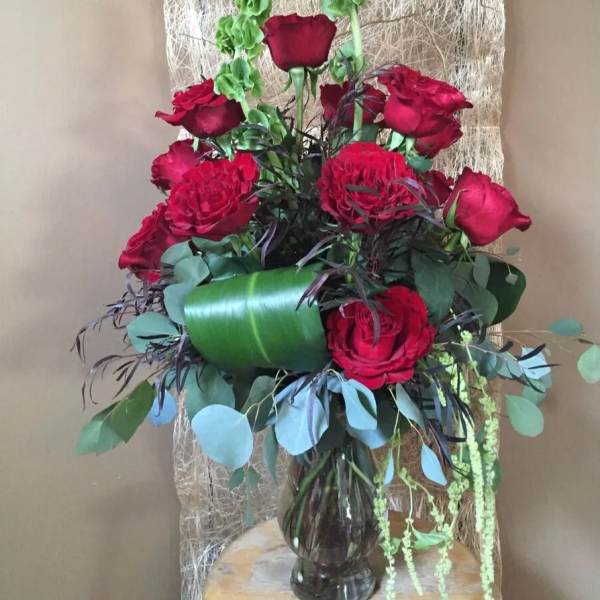 Red roses arranged in a glass vase with mixed greenery