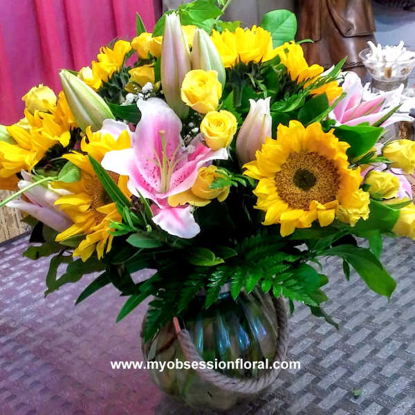 Bouquet of yellow sunflowers, pink lilies, and yellow roses in a glass vase