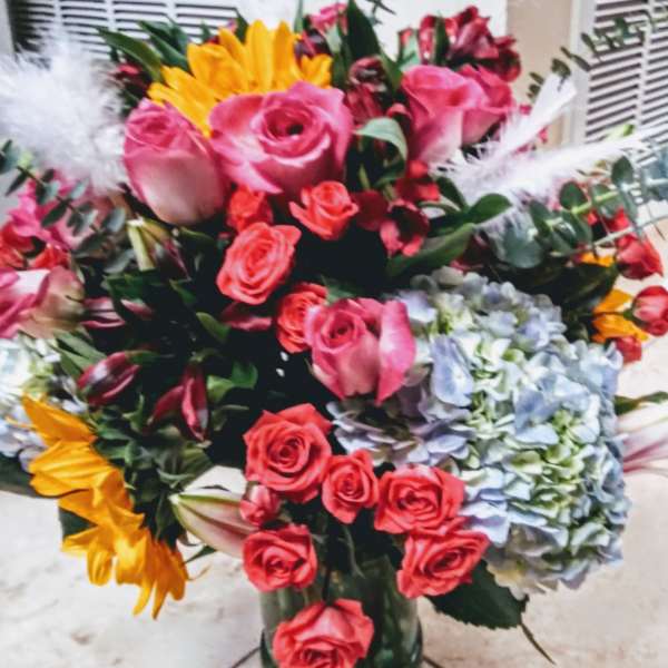 Bouquet of pink and red roses with sunflowers and hydrangeas in a glass vase