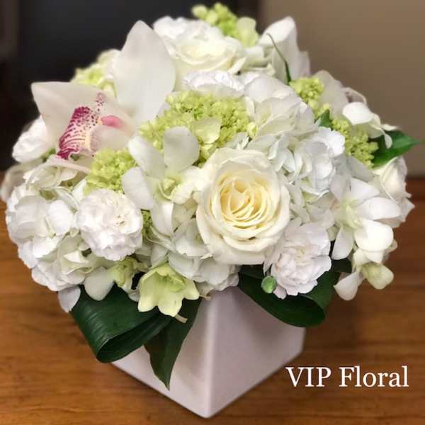 White floral arrangement in a square vase with pale green accents