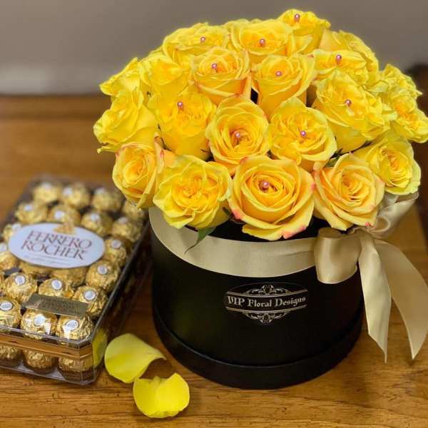 Yellow roses in a black hatbox beside a box of Ferrero Rocher chocolates
