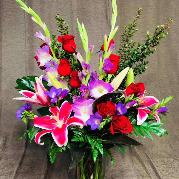 Bouquet of red roses, pink lilies, and purple flowers in a glass vase