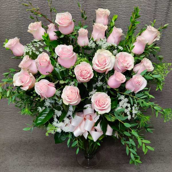 Pink roses arranged in a clear glass vase with a ribbon bow