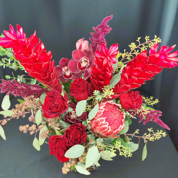 Red tropical bouquet with orchids, roses, and protea in a vase