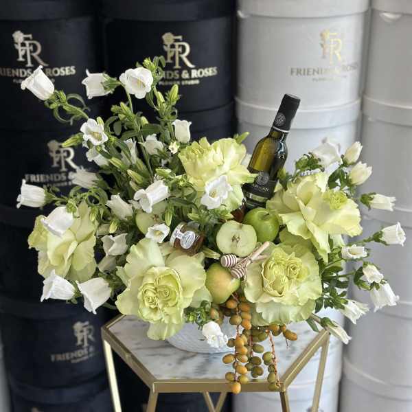 White and pale green floral arrangement with wine bottles and apples in a bowl